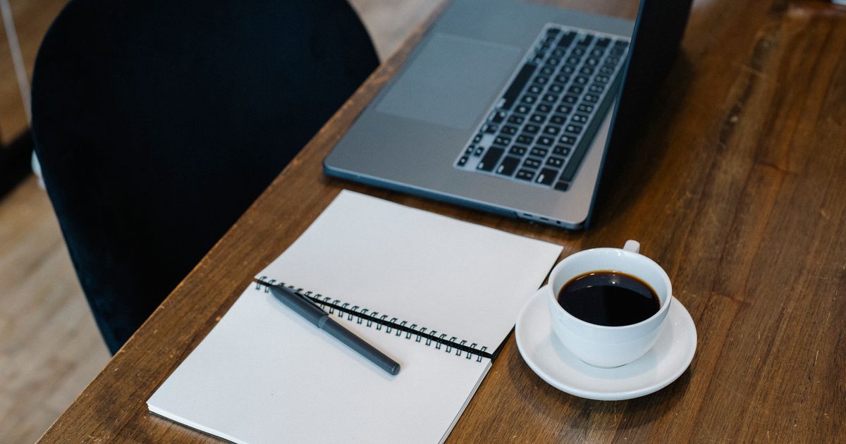 Open laptop and notebook beside a cup of coffee on a wooden table
