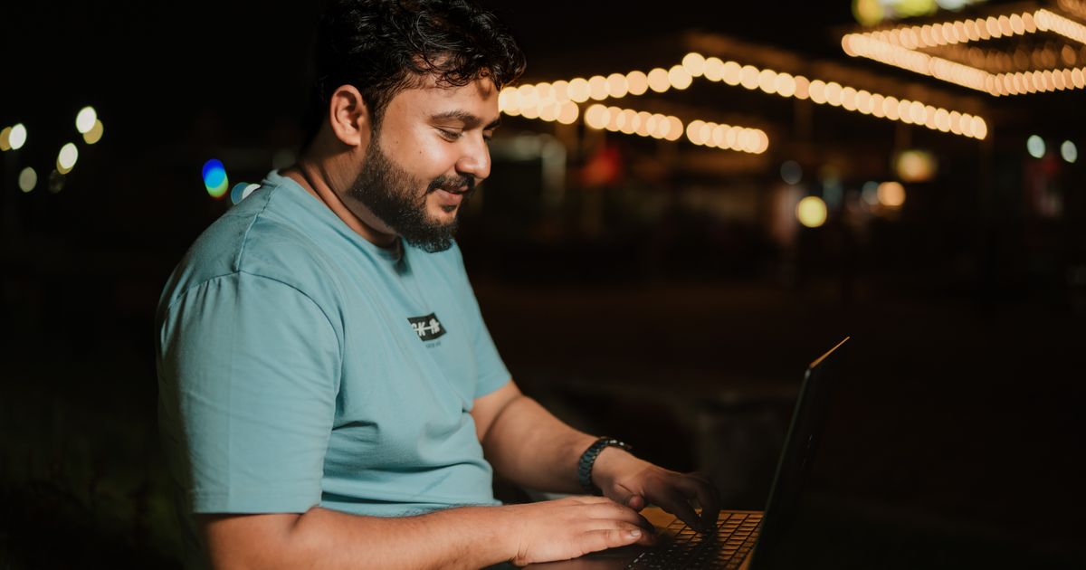Man typing on a laptop outdoors at night under string lights